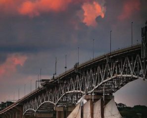 Sunset clouds and an arched bridge over a river with a sailing boat passing beneath