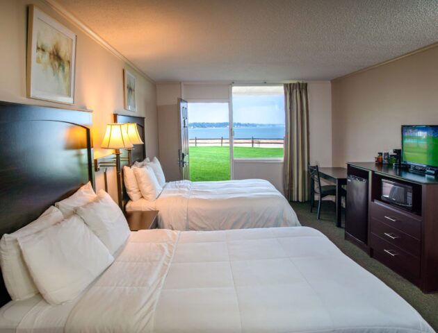 A spacious Yorktown hotel room with colonial green carpet, two queen beds, a desk, and waterfront views.