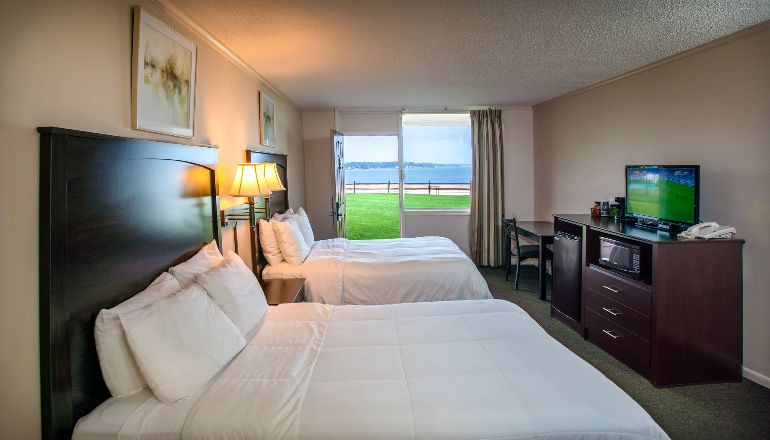 A spacious Yorktown hotel room with colonial green carpet, two queen beds, a desk, and waterfront views.