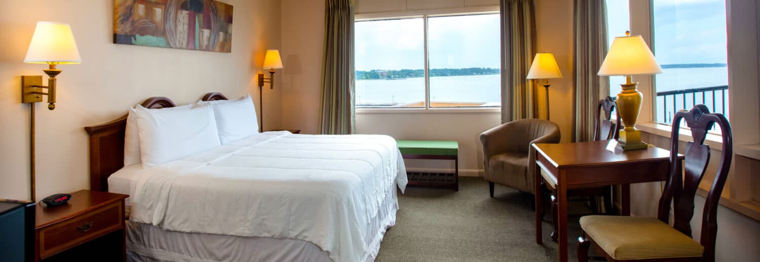 A spacious Yorktown hotel room with colonial green carpet, a king bed with white linens, a desk, and waterfront views.