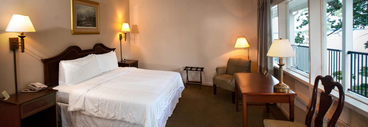 A spacious Yorktown hotel room with colonial green carpet, a king bed with white linens, a desk, and accent lighting.