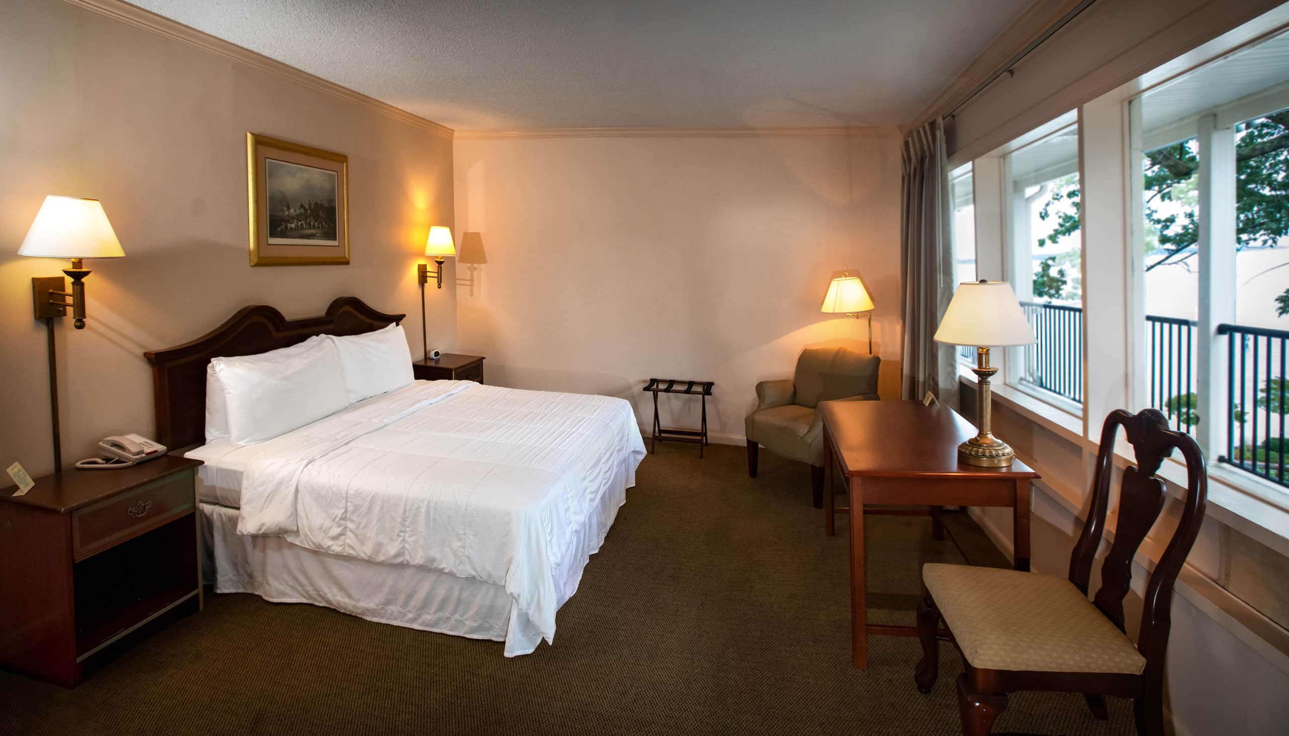 A spacious Yorktown hotel room with colonial green carpet, a king bed with white linens, a desk, and accent lighting.