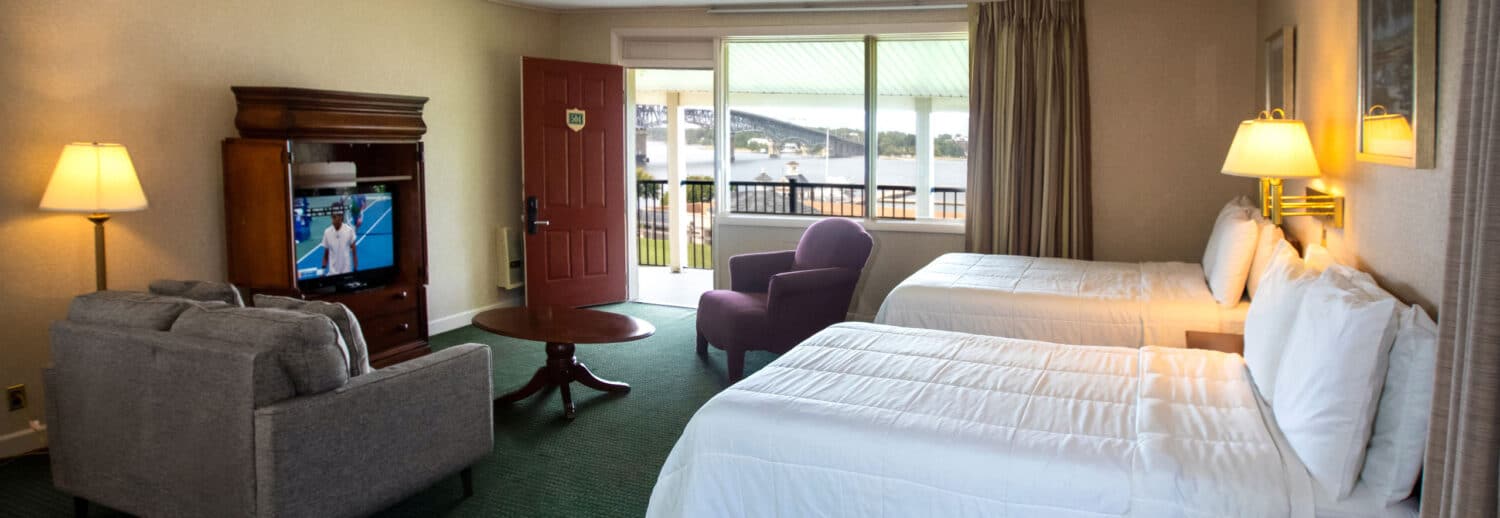 A spacious Yorktown hotel room with colonial green carpet, two full beds, a sofa set, and a TV.