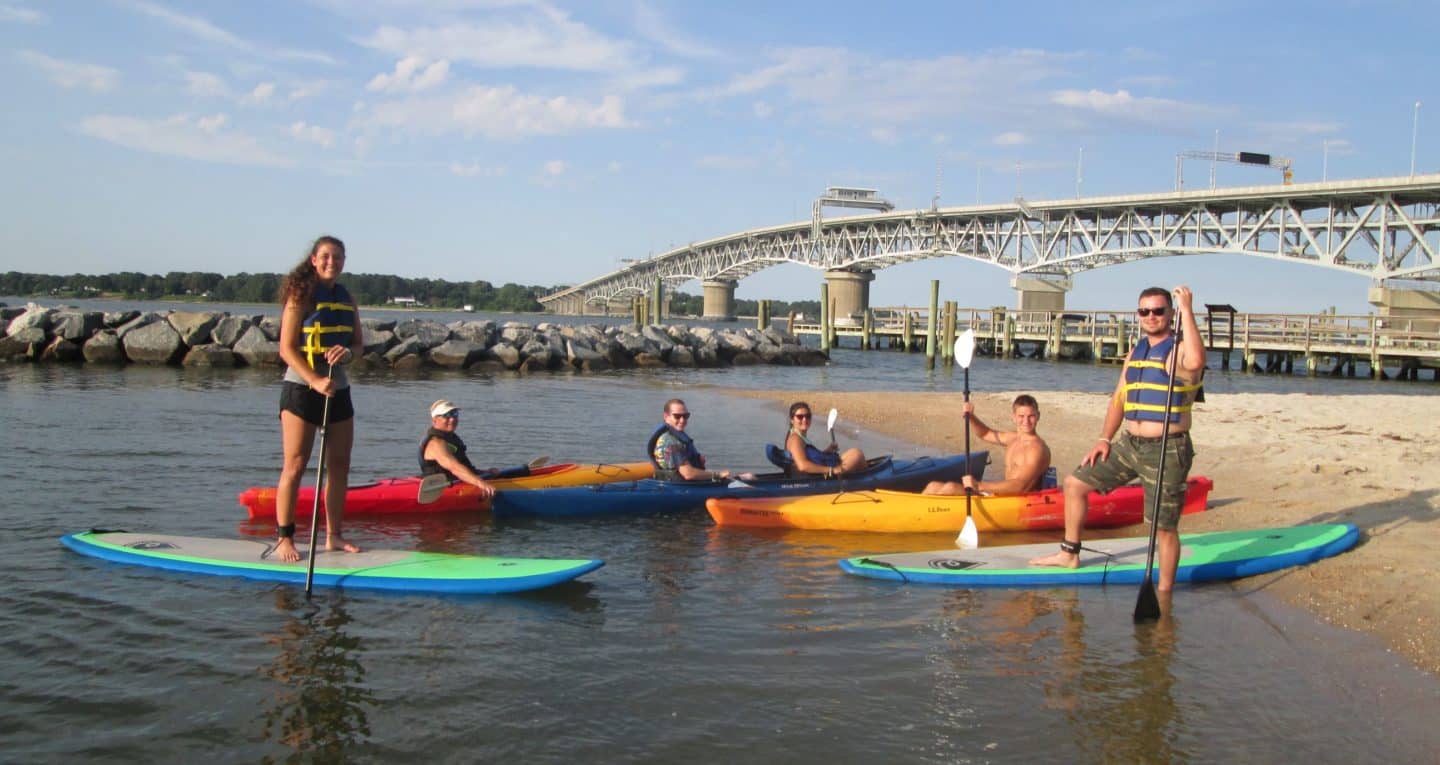 Family in kayaks on a beach with an arched bridge in the background