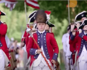 Reenactors dressed in Revolutionary War outfits marching with flag and fife