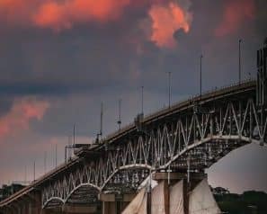 Sunset clouds and an arched bridge over a river with a sailing boat passing beneath
